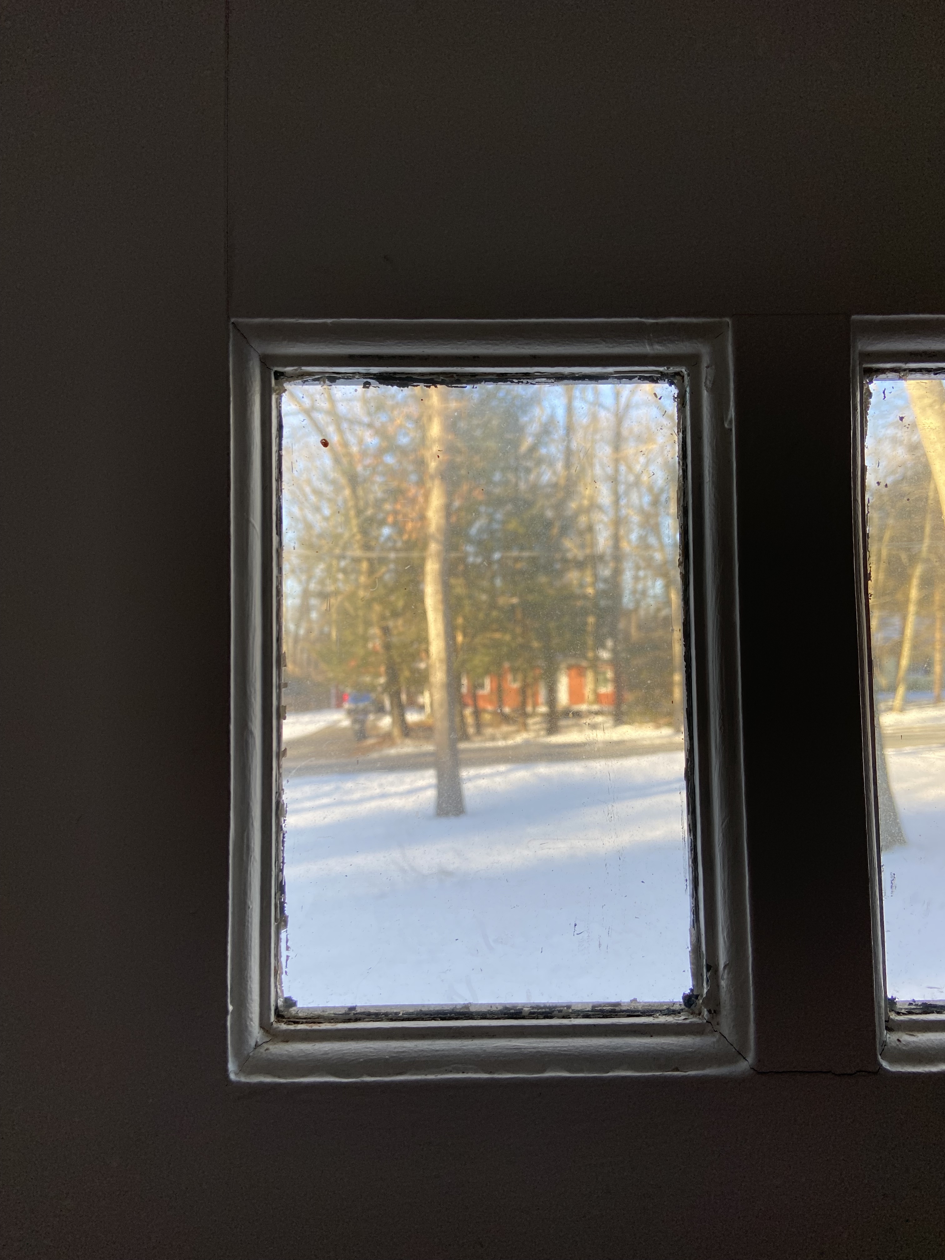 This is an image out of a small window to the front yard covered in snow. There is a red house in the background and a tree in the middle ground