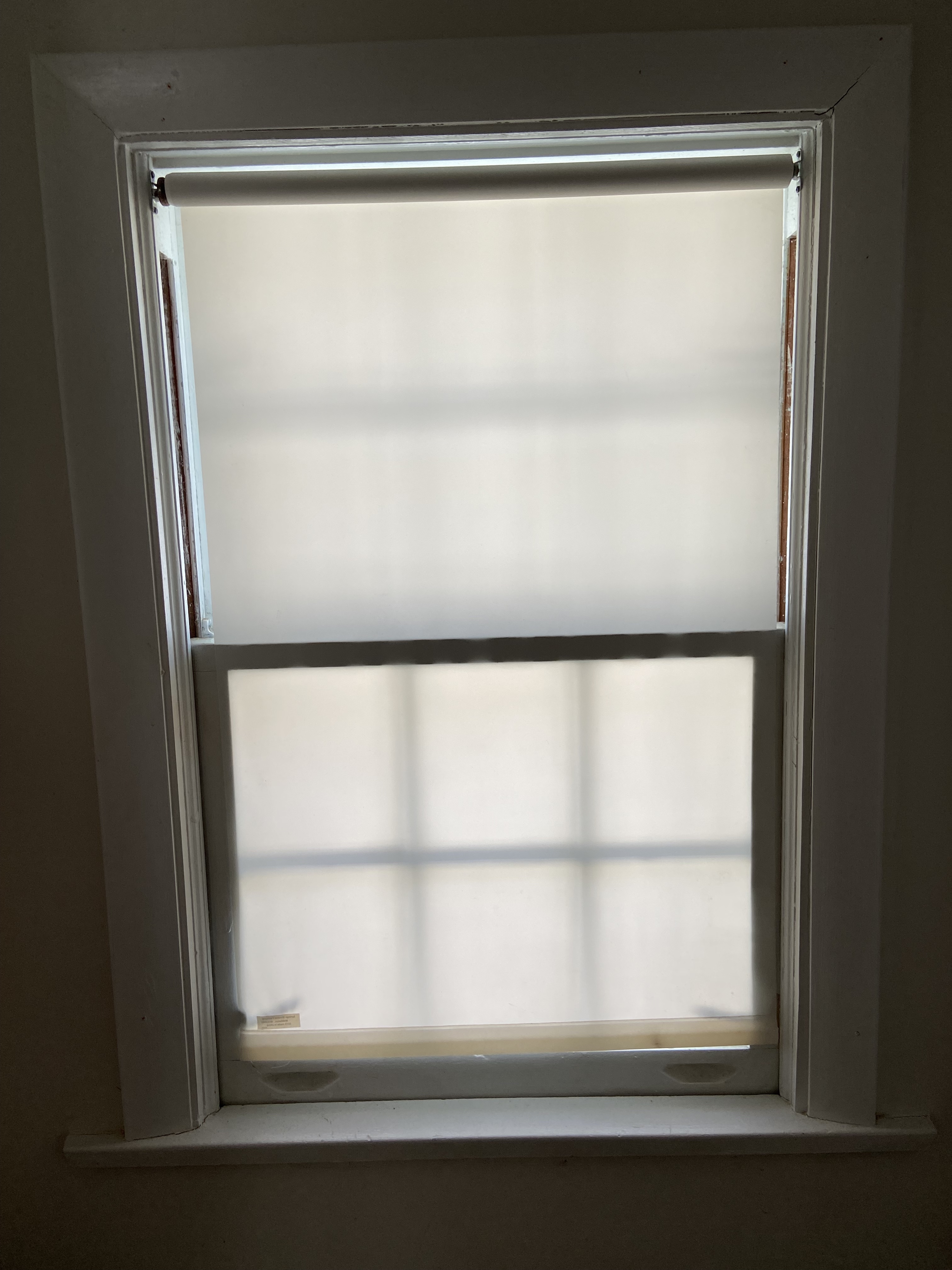 This is an image of a closed window. There is a white rollershade covering the window. 